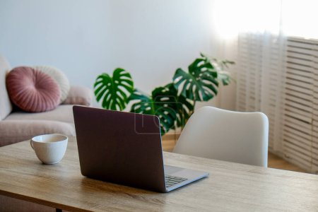 Espacio de trabajo creativo del bloguero. Ordenador portátil en mesa de madera en la oficina de estilo loft con paredes blancas y palmera monstera en el suelo. Concepto de mesa del diseñador. Cerrar, copiar espacio, fondo