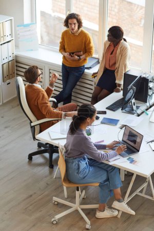 Photo for Vertical high angle view at multi-ethnic IT development team collaborating on business project while working in software production studio - Royalty Free Image