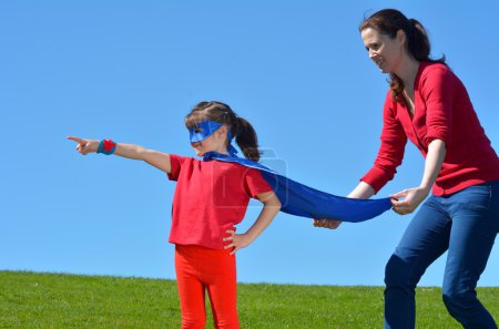 Foto de Madre superhéroe mostrar a su hija cómo ser un superhéroe contra el fondo del cielo azul con espacio de copia. concepto de foto de Super héroe, el poder de la chica, el juego de simular, la infancia, la imaginación. Gente real - Imagen libre de derechos