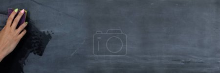 Panoramic frame for a womans hand wiping the blackboard with a wet sponge before the next lessons in the classroom. Prepares a place for writing on a school blackboard.