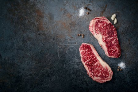 Dos filetes de ternera de mármol Wagyu crudos y frescos, lomo de tira sobre un fondo de piedra oscura, vista superior y espacio para copiar