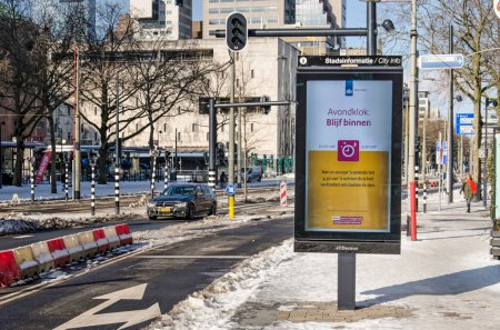 Téléchargez les photos : Rotterdam, Pays-Bas, 14 février 2021 : Panneau électronique annonçant le couvre-feu comme mesure covid-19 sur le boulevard Coolsingel partiellement enneigé - en image libre de droit