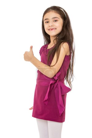 Photo for Elegant little dark-haired girl with long hair in a short fashion velvet dress and white stockings stretched out a hand with a raised thumb, the gesture is all right or hitchhiking. The girl smiles - Royalty Free Image