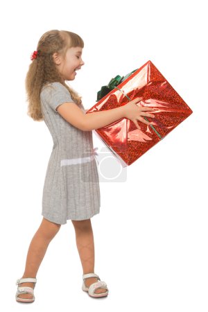 Photo for Joyful little girl blonde in a Warm grey dress. The girl turned sideways to the camera she holds in her hands a big box with a gift  -Isolated on white background - Royalty Free Image