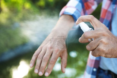 Hombre aplicando repelente de insectos en la mano al aire libre, primer plano Hombre aplicando repelente de insectos en la mano al aire libre, primer plano