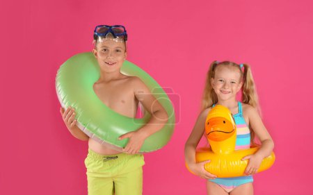 Foto de Lindos niños pequeños en ropa de playa con anillos inflables brillantes sobre fondo rosa - Imagen libre de derechos