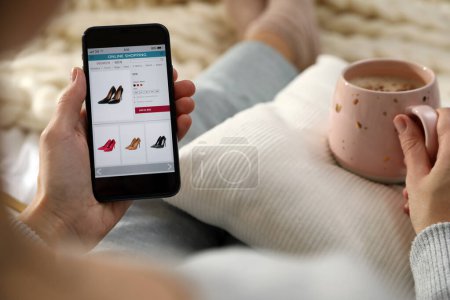 Mujer con taza de café con teléfono inteligente para las compras en línea a cuadros, primer plano Mujer con taza de café con teléfono inteligente para las compras en línea a cuadros, primer plano