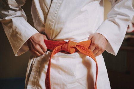 Male karate in white kimono hold on to red belt.