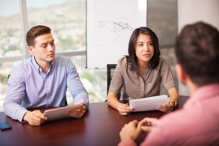 Foto de Un par de latinos con currículum en las manos, entrevistando a un candidato de trabajo en una sala de reuniones - Imagen libre de derechos