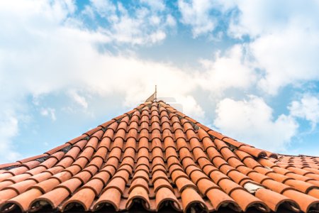 Photo for Old tiled roof. Top of building. Architecture of europe. Blue sky with white clouds in background. Sun glow. - Royalty Free Image