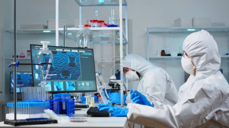 Científico en traje ppe sosteniendo tubo de ensayo con líquido azul en laboratorio estéril