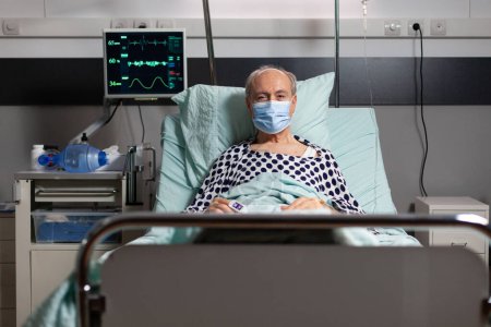 Photo for Portrait of sick senior man patient with chirurgical mask resting in hospital bed, with iv drip attached on hand having oximeter attached on finger. Modern medical equipment. - Royalty Free Image