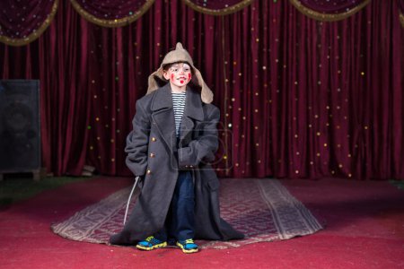 Photo for Talented boy standing and holding a sword while wearing oversized retro gray coat and Russian hat over modern casual clothes during theatrical play on stage - Royalty Free Image