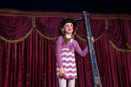 Téléchargez les photos : Fille portant robe rayée et casque de combat debout sur scène tenant des barils de fusil de chasse droit soutenu sur scène avec rideau rouge - en image libre de droit