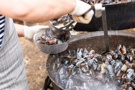Persona que sirve mejillones preparados de maceta grande
