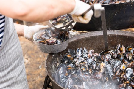 Photo for Close Up of Person Serving Single Portion of Hot Steaming Mussels from Large Pot into Take Out Container - Royalty Free Image