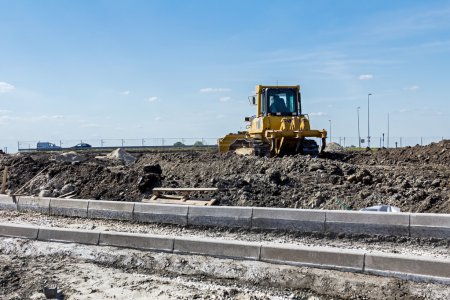 Photo for Construction site, the roadside stones are lined and placed on gravel. Earthmover with caterpillar is moving earth in background. - Royalty Free Image