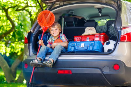 Kleiner Junge sitzt im Kofferraum des Autos, kurz bevor er in den Urlaub fährt