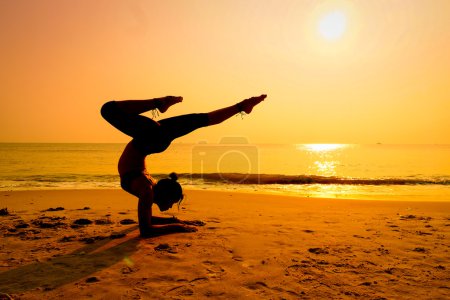 Foto de Silueta joven practicando yoga en la playa al amanecer - Imagen libre de derechos