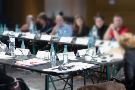 vasos y botellas en la mesa de conferencias y personas en el fondo
