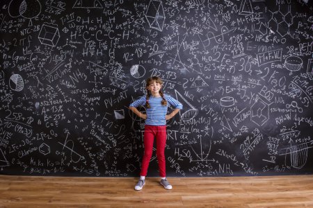 Téléchargez les photos : Petite fille mignonne à l'école devant un grand tableau noir - en image libre de droit