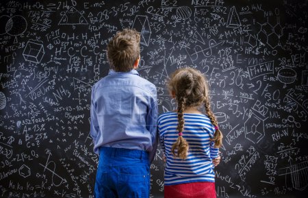 Photo for Cute little boy and girl in front of a big blackboard. Studio shot on black background - Royalty Free Image