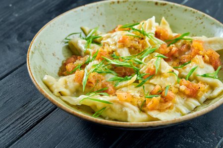 Photo for Traditional dish of Israeli cuisine - chicken kreplach with tomato salsa and green onions in a plate on a black wooden background. Restaurant food. Dumplings with different fillings - Royalty Free Image