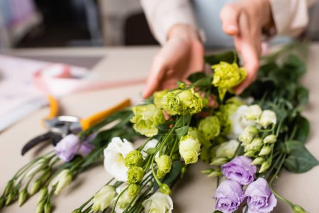 partial view of florist making bouquet with eustoma in flower shop on blurred background