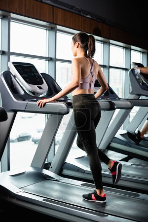 athletic sportswoman in leggings running on treadmill in sports center