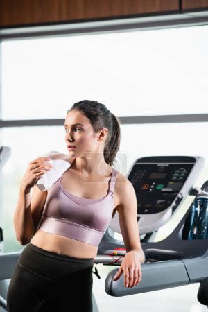 young sportswoman looking away while standing on treadmill 