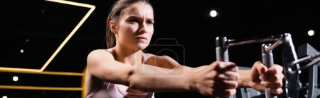 athletic sportswoman exercising on rowing machine on blurred foreground, banner