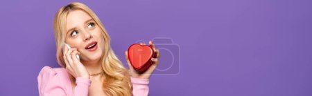 mujer joven rubia con corazón rojo en forma de caja hablando en el teléfono inteligente sobre fondo púrpura, pancarta mujer joven rubia con corazón rojo en forma de caja hablando en el teléfono inteligente sobre fondo púrpura, pancarta