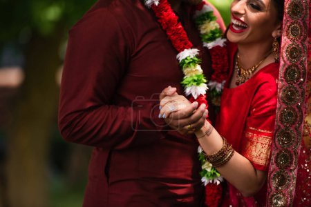 cropped view of indian man holding hands with cheerful bride in sari