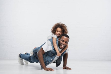 alegre africano americano hombre haciendo flexiones con feliz hija piggybacking él en gris alegre africano americano hombre haciendo flexiones con feliz hija piggybacking él en gris