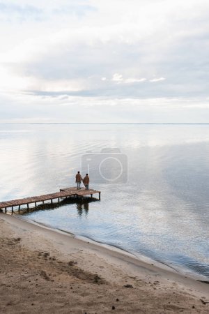 Vista trasera de pareja en mantas de pie en el muelle cerca del mar 