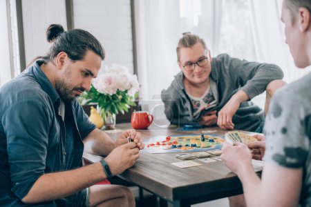 Los amigos juegan un juego de mesa en el salón. La compañía de chicos jóvenes se sienta en una mesa y emocionalmente y alegremente juega un juego de cartas en el fin de semana