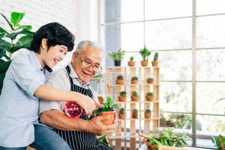 Asiático abuelo jubilación y su nieto con sonrisas, pasar tiempo de calidad juntos por disfrutar de cuidar de las plantas por pulverización de agua en un jardín interior. Vinculación familiar entre viejos y jóvenes.