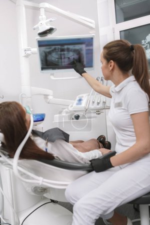 Inyección vertical de un dentista que explica la radiografía dental de su paciente en la pantalla, esperando que funcione la sedación por inhalación
