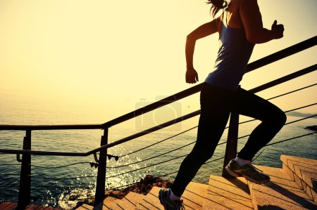 Foto de Estilo de vida saludable mujer deportiva corriendo por las escaleras de piedra amanecer junto al mar - Imagen libre de derechos