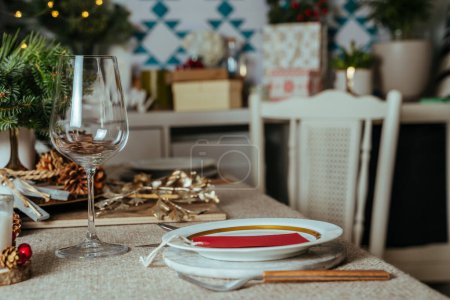 Homely christmas table setting, decorated with pine branches and rustic tablecloth in the living room of home in European style, with Christmas lights.