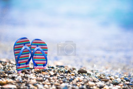 Kids flip flops on beach in front of the blue sea