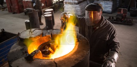 Steel worker in protective clothing raking furnace in an industr