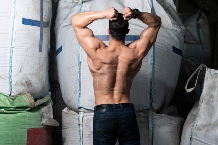 Hombre guapo de pie fuerte en el almacén con grandes bolsas y músculos de flexión - Muscular atlético culturista Fitness Model Posing