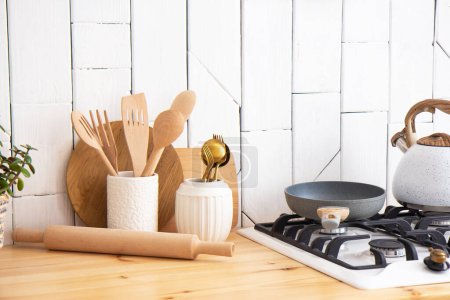 Kitchen utensils and wooden dishes and a green indoor plant in a pot on a wooden shelf