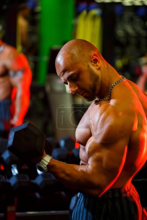 Photo for Muscular shirtless man doing biceps exercises with dumbbell exercises as part of his bodybuilding workout. Fitness motivation, sports lifestyle, health, athletic body - Royalty Free Image