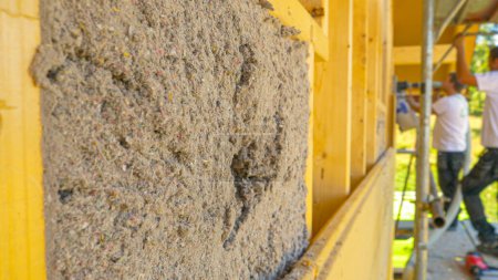 Photo for CLOSE UP: A group of workers blow cellulose insulation into the wooden walls framing of a modern house under construction. Contractors insulate the outer walls of a large ecofriendly housing project. - Royalty Free Image