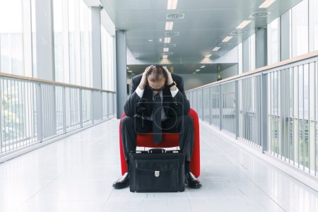 Photo for Desperate Business man suffering with head in his hands; lobby background - Royalty Free Image