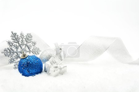 Photo for Decoration of silver and blue glitter baubles with ribbon and snowflake on snow on white background - Royalty Free Image