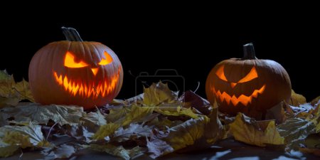 Foto de Espeluznante dos calabazas como gato o linterna entre hojas secas sobre fondo negro - Imagen libre de derechos