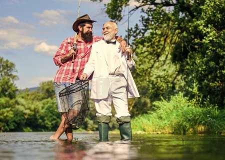 Foto de Está listo para la pesca. padre jubilado e hijo maduro con barba. amigos hombres con caña de pescar y red. hobby del hombre de negocios. pesca de jubilación. pescadores felices en el agua. Aventuras de pesca con mosca. - Imagen libre de derechos